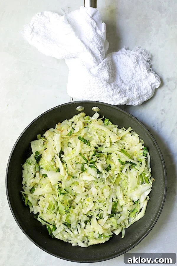 Sautéed green cabbage and onions, softened and fragrant, cooking in a nonstick skillet.