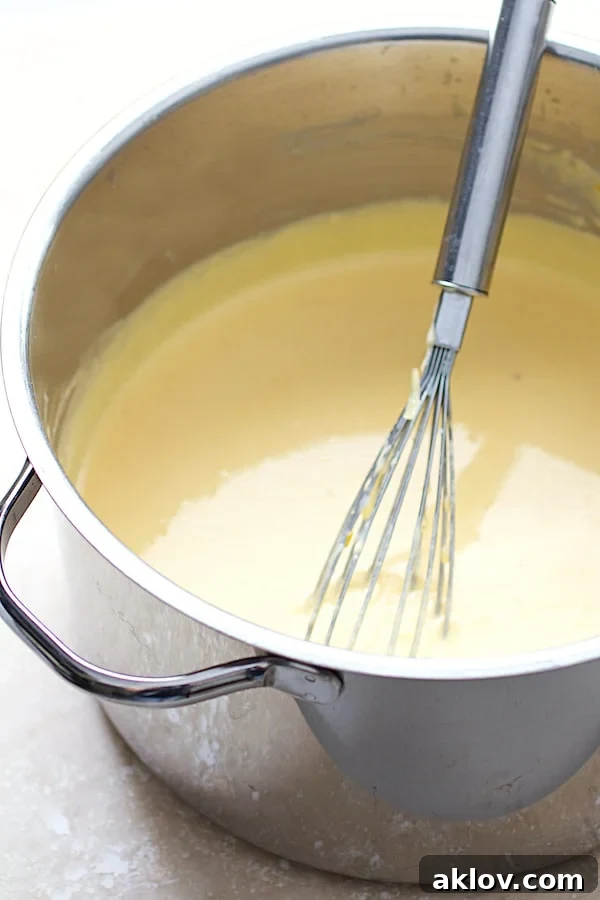 Creamy cheddar cheese sauce being whisked in a stainless steel saucepan, smooth and lump-free.