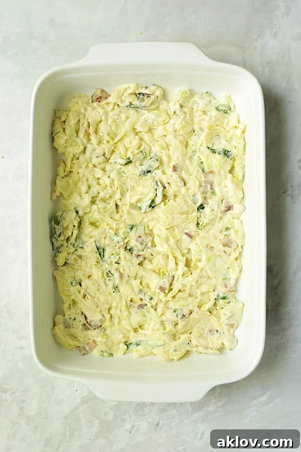 First layer of creamy cabbage mixture spread in a white rectangular baking dish, ready for potatoes.