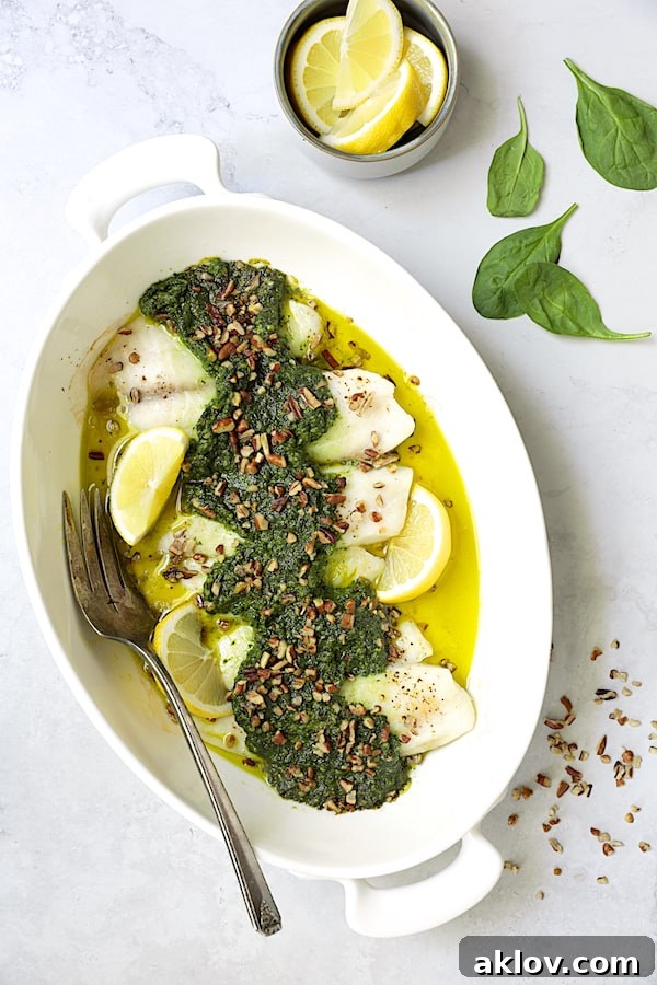 Photo of Baked Tilapia with Spinach Pecan Pesto in white baking dish with serving fork, highlighting the vibrant colors and appealing presentation.
