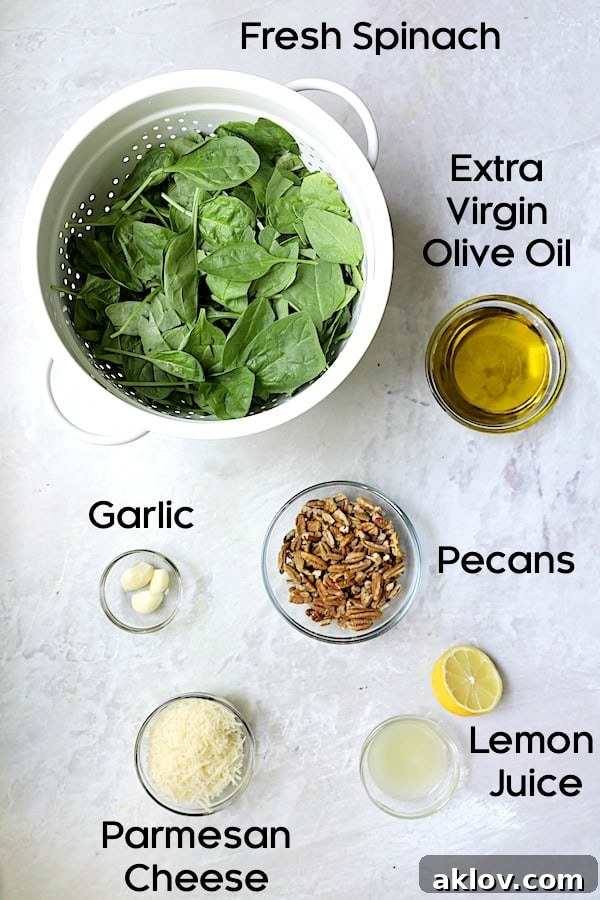 Photo of ingredients for Spinach Pecan Pesto, neatly arranged before blending. Includes fresh spinach, garlic, pecans, olive oil, Parmesan, and a lemon.