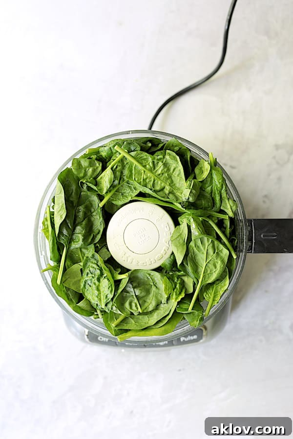 Photo of spinach leaves in food processor, ready to be blended into pesto.