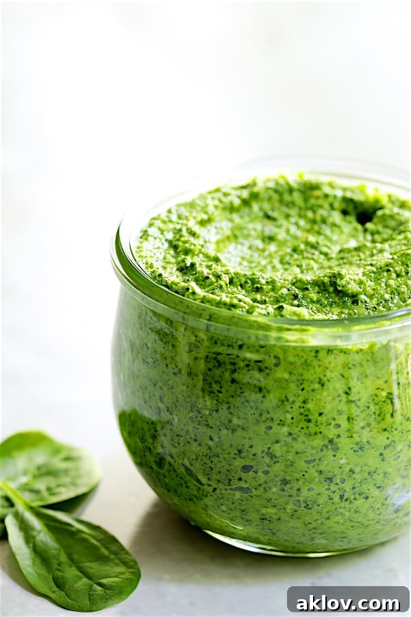 Photo of bright green Spinach Pecan Pesto stored in a clear glass jar, showing its rich texture.