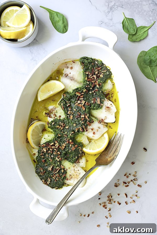 Photo of Baked Tilapia with Spinach Pecan Pesto on light gray background garnished with pecans and lemon wedges, showcasing a beautifully cooked dish.
