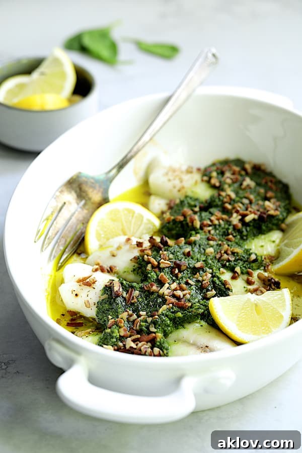 Photo of Baked Tilapia with Spinach Pecan Pesto in white baking dish with serving fork, demonstrating the flaky texture.