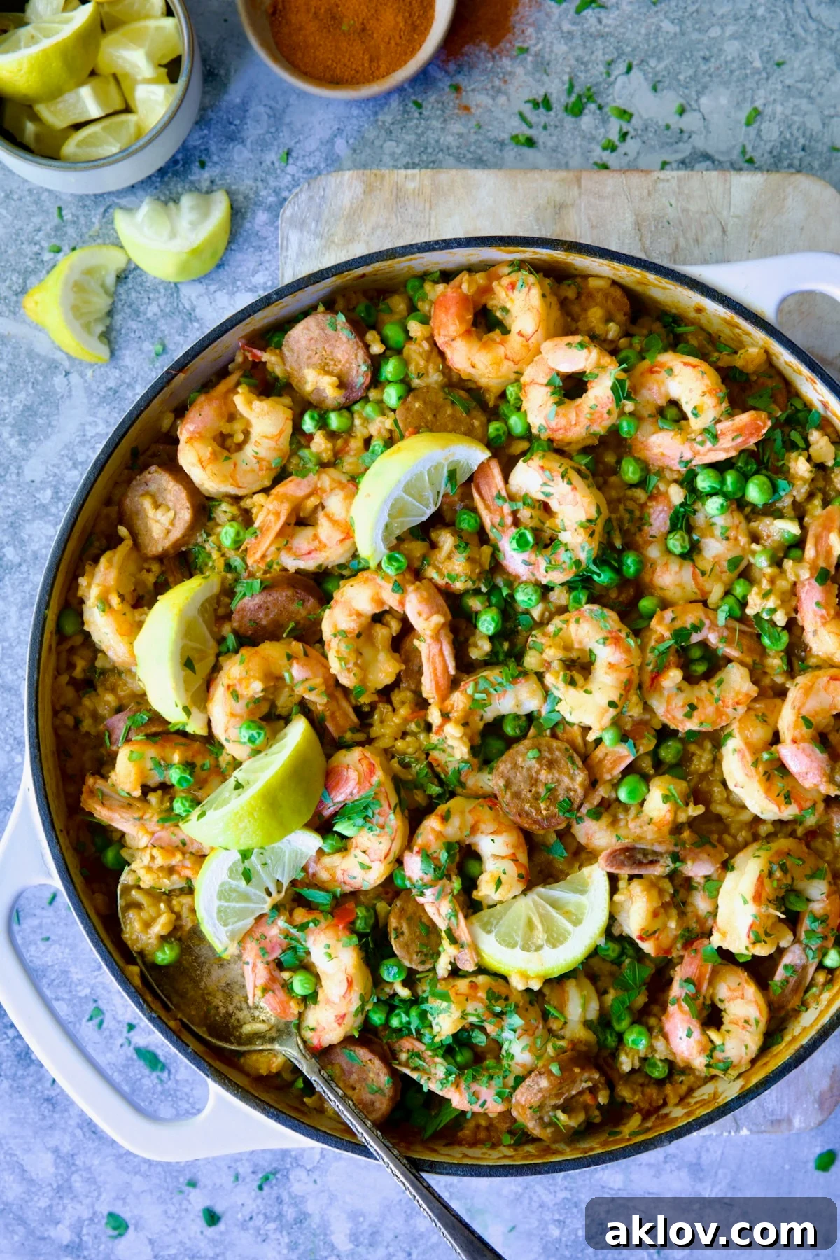 Brown Rice Paella with Shrimp and Chorizo in white enamel cast iron skillet on wood cutting board.