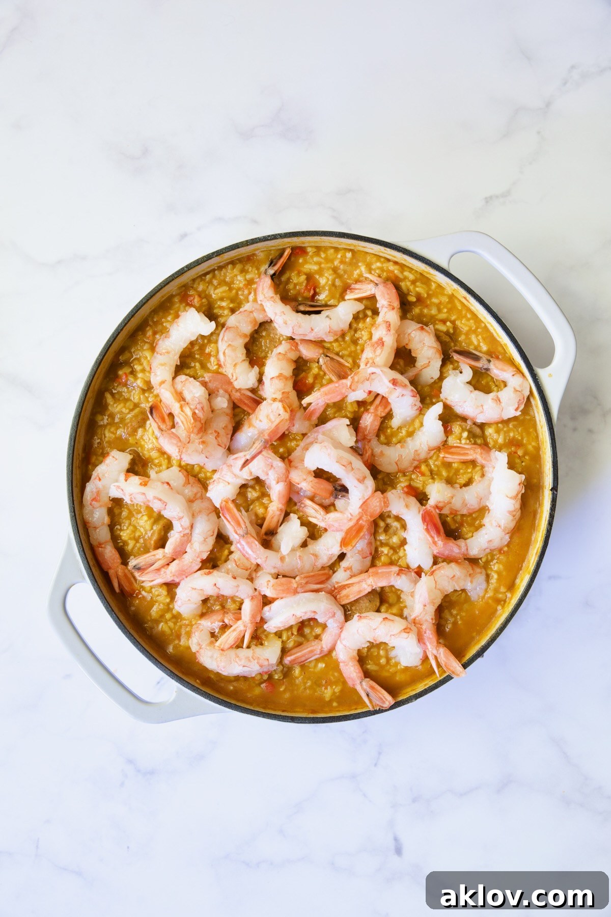 Process shot of paella with shrimp added.