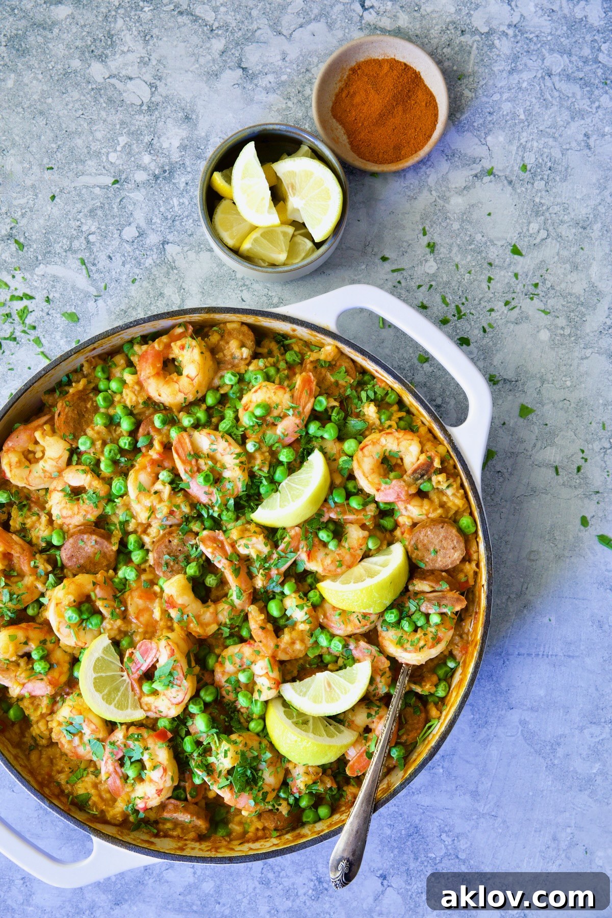 Skillet of Brown Rice Paella with Shrimp and Chorizo with lemon wedges and bowl of paprika.