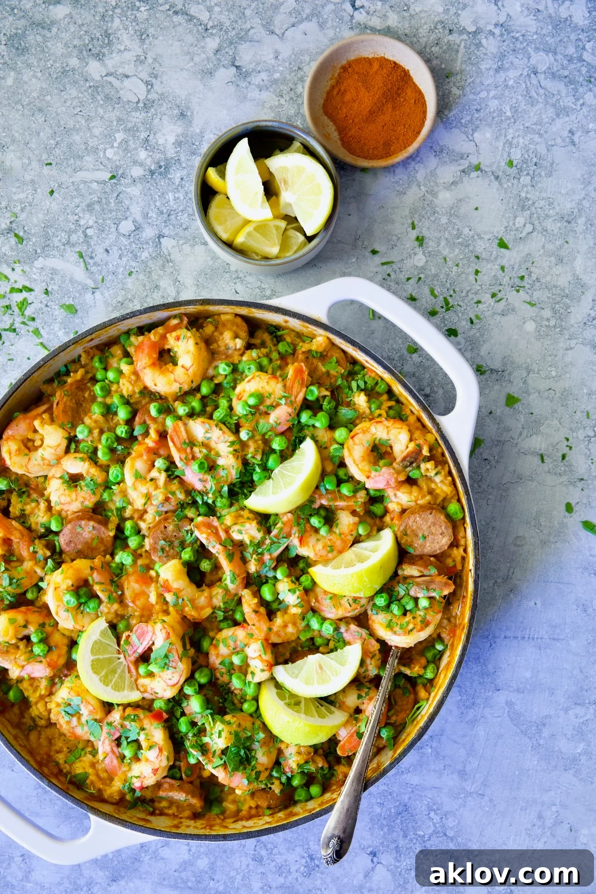 Skillet of Brown Rice Paella with Shrimp and Chorizo with lemon wedges and a small bowl of paprika, beautifully presented.