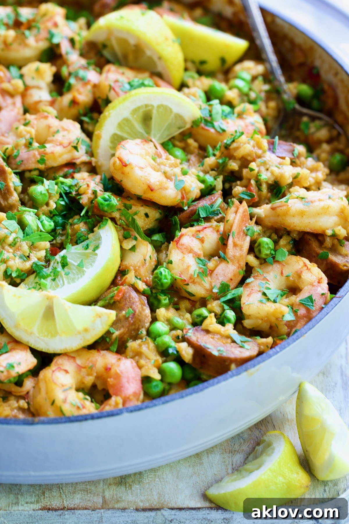 Brown Rice Paella with Shrimp and Chorizo with lemon wedges in white cast iron enamel skillet, showing the full spread.