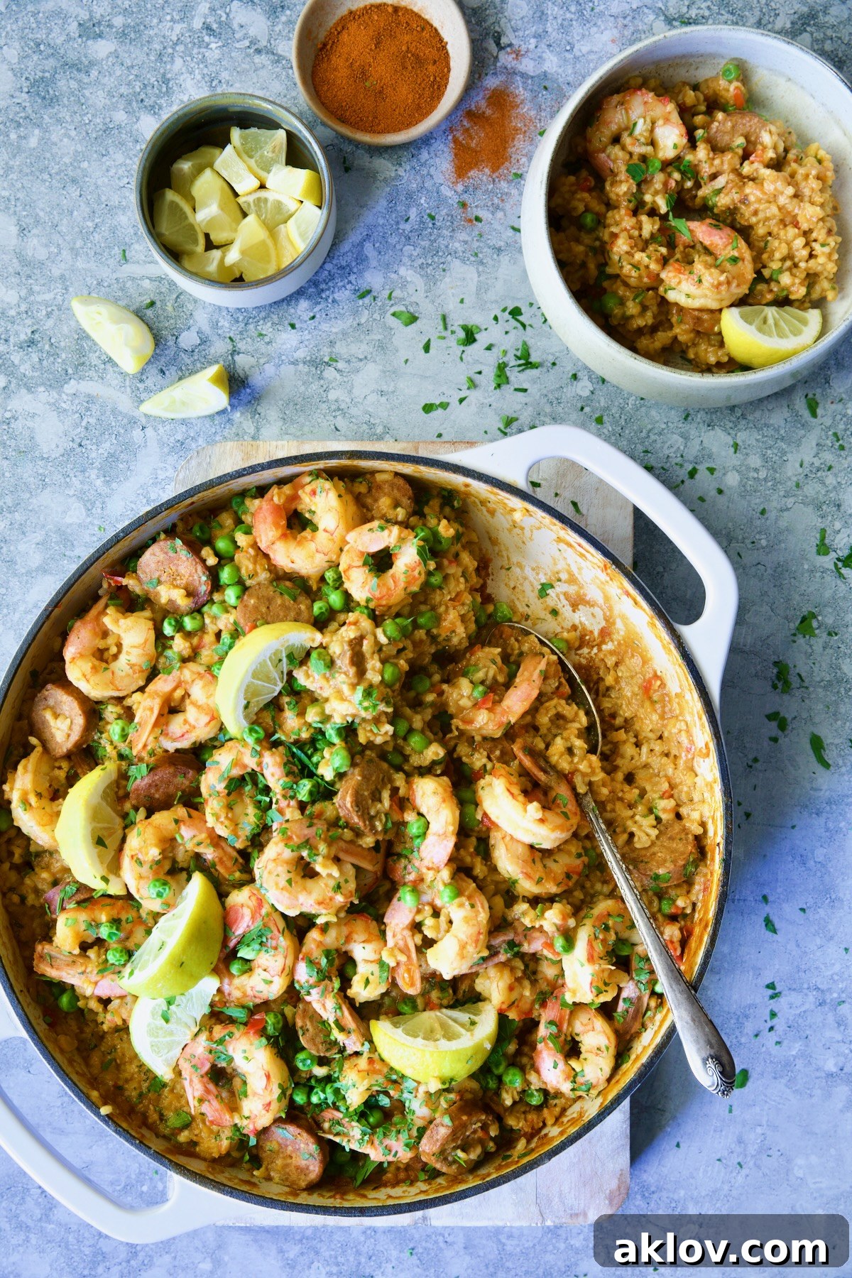 Pan of paella garnished with lemon wedges with some served into an individual bowl.