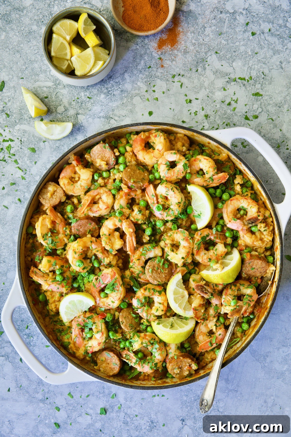 Brown Rice Paella with Shrimp and Chorizo with lemons in white enamel cast iron skillet.