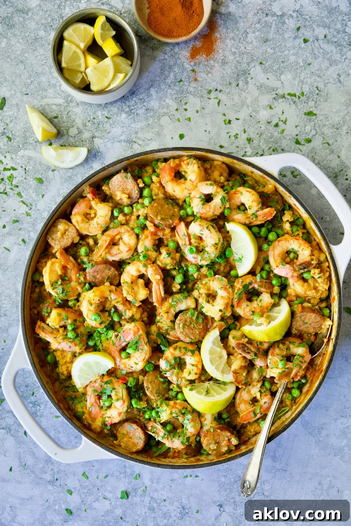Brown Rice Paella with Shrimp and Chorizo with lemons in white enamel cast iron skillet, presenting a delicious meal.