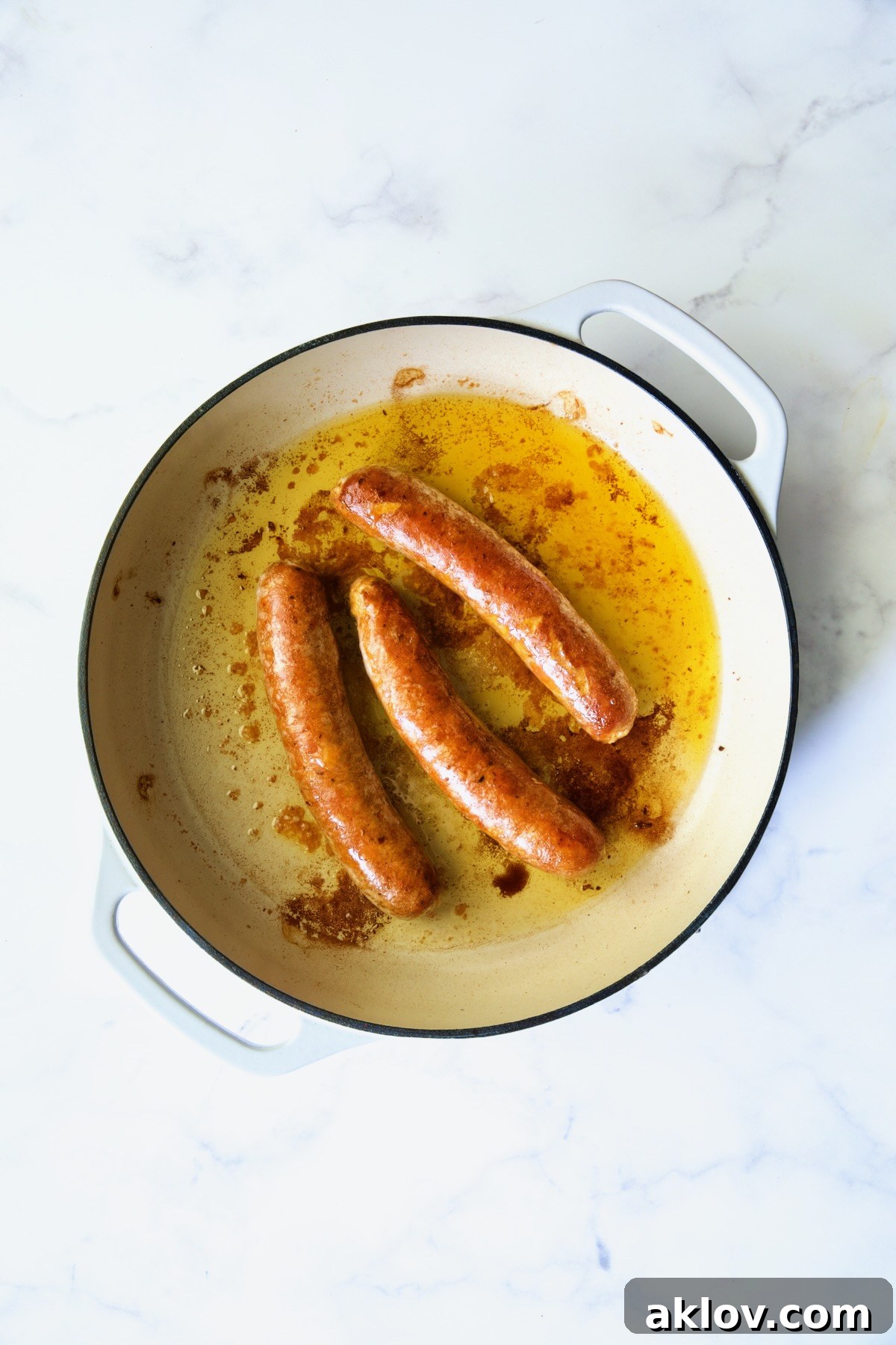 Three cooked chorizo links in white enamel cast iron skillet.