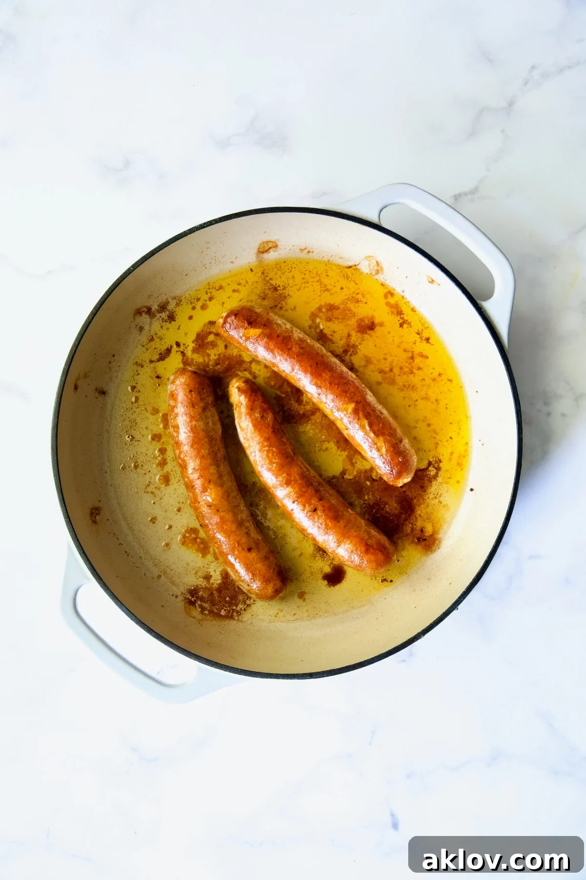 Three cooked chorizo links in white enamel cast iron skillet, browned and ready for slicing.