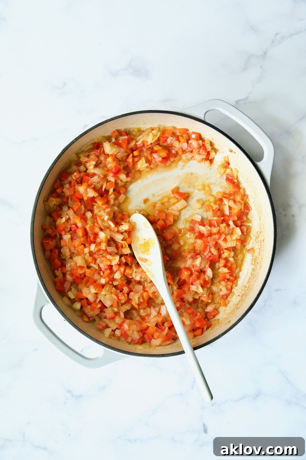 Process shot of cooked onions, bell pepper and tomatoes.