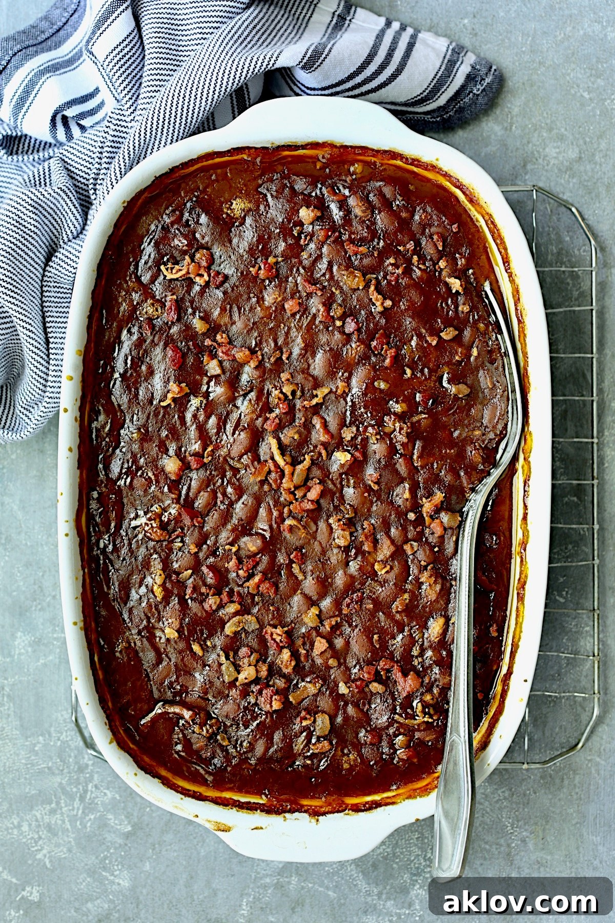 Kicked-Up Canned Baked Beans on cooling rack with serving spoon with blue striped towel.