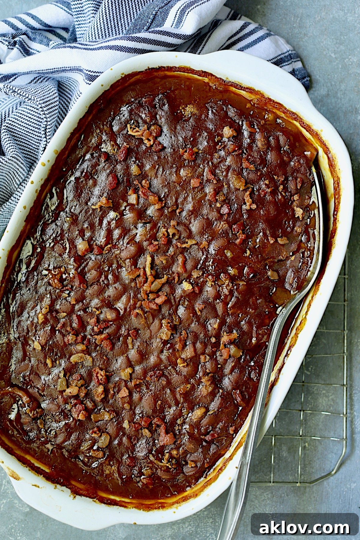 Baking dish full of baked beans with serving spoon.
