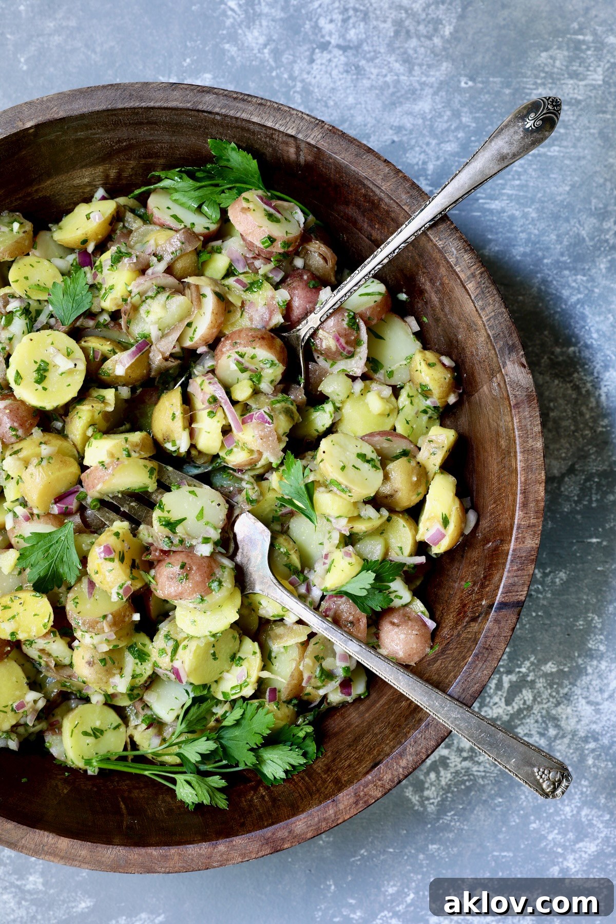 A beautifully presented French Potato Salad in a rustic wooden bowl, garnished with fresh parsley and ready to be served.