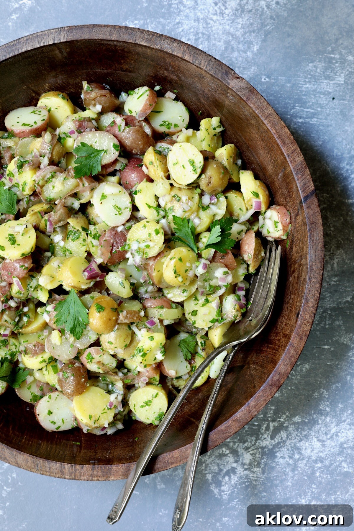 A simple yet elegant dark wooden bowl filled with French Potato Salad, ready to be enjoyed, emphasizing its natural beauty.