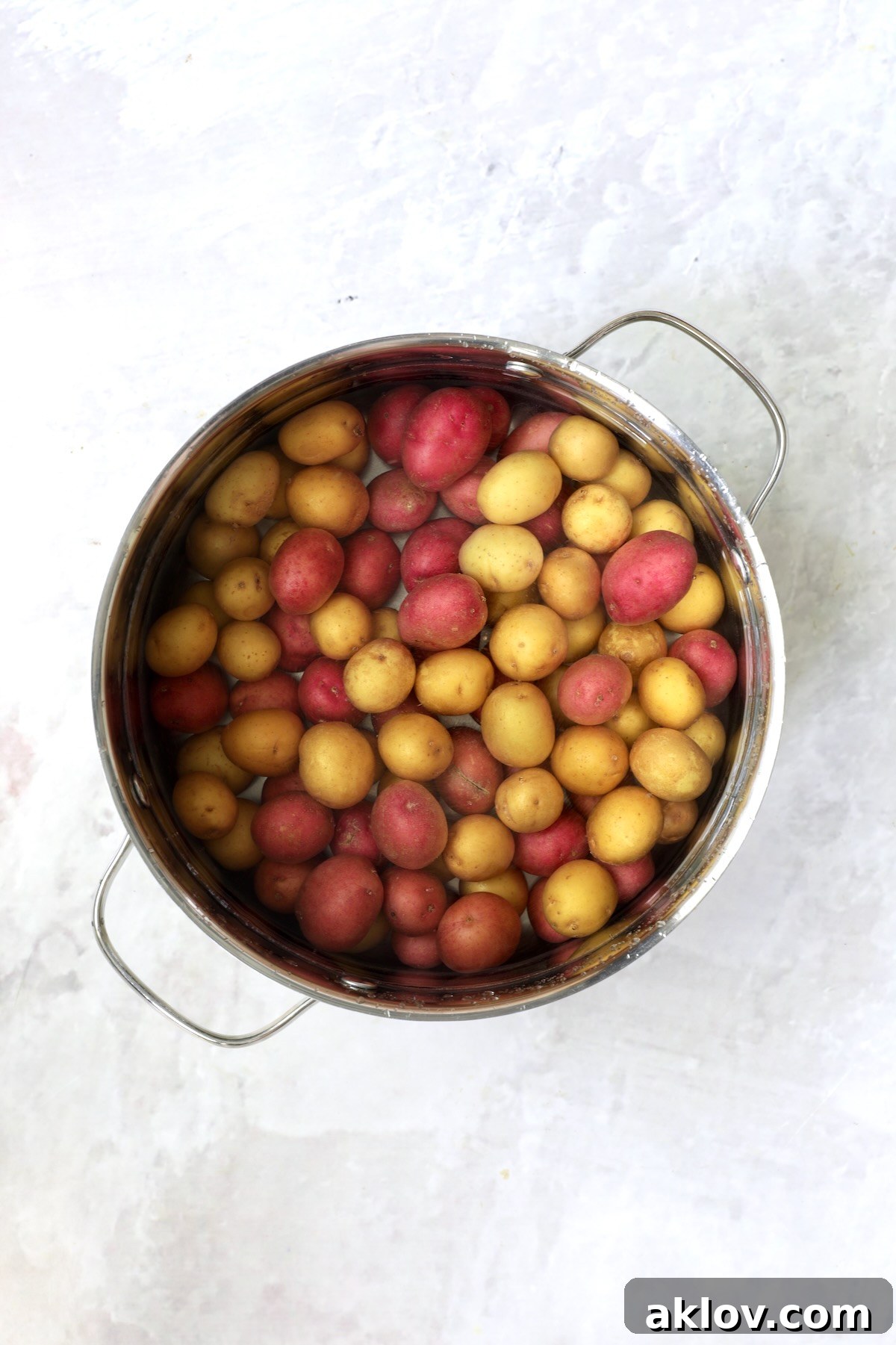 Red and yellow new potatoes submerged in water in a stainless steel pot, ready for boiling.