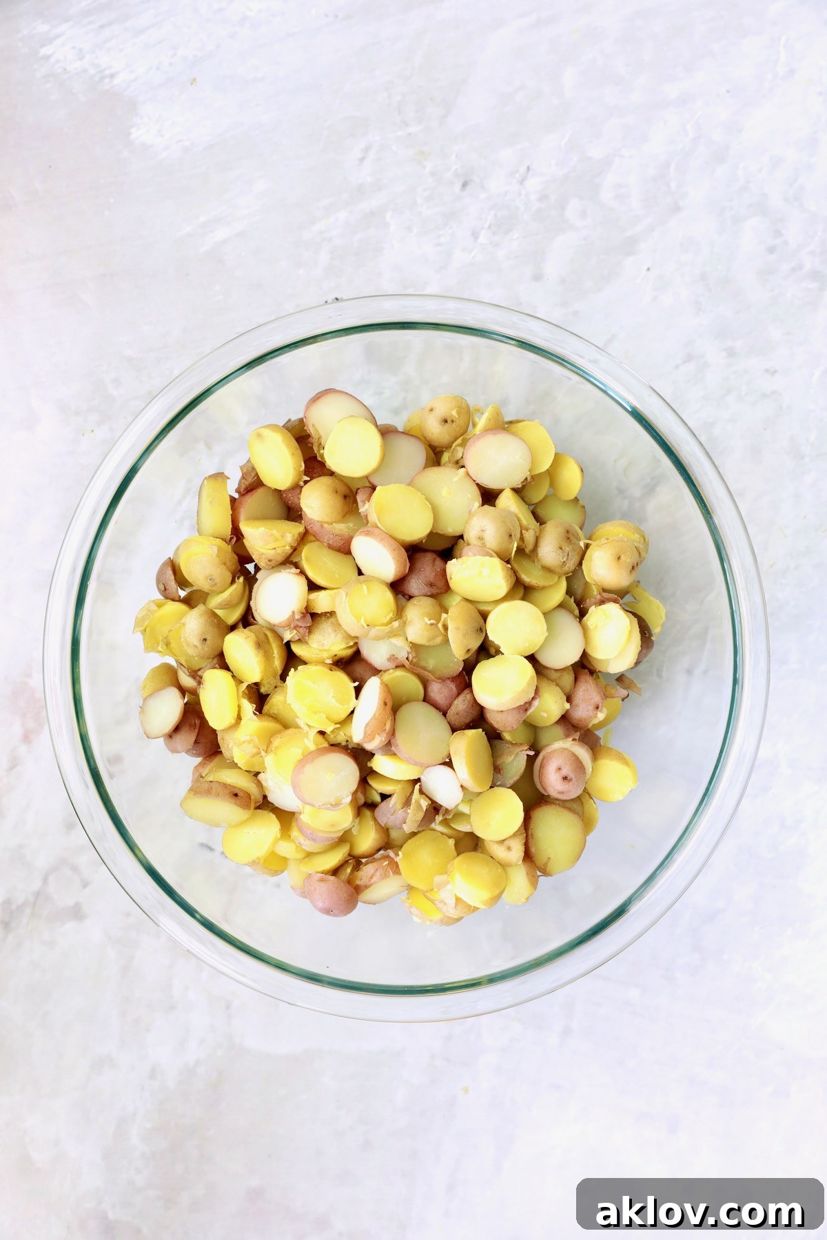 Freshly sliced, cooked red and yellow new potatoes neatly arranged in a clear glass bowl, ready for the next step.