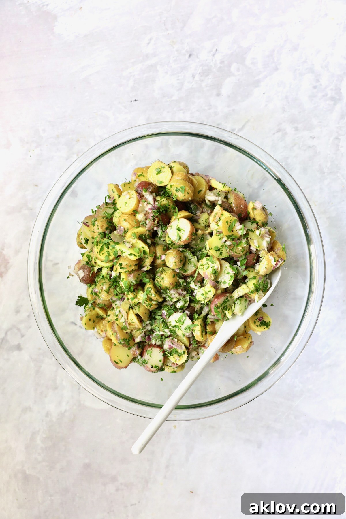 The fully dressed French Potato Salad, mixed with fresh herbs and vinaigrette, in a large glass bowl.
