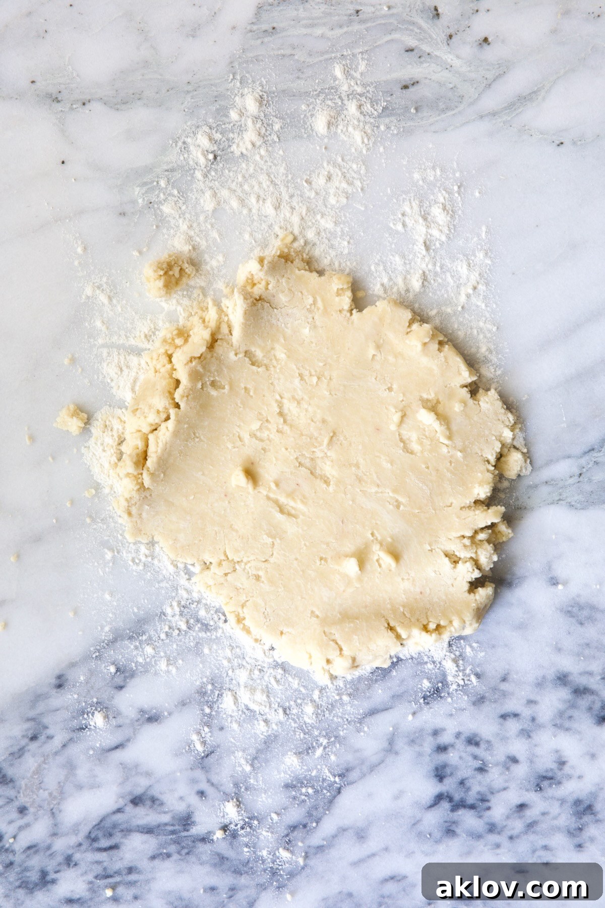 Galette dough partially rolled out on a white marble pastry board, showcasing its smooth texture and readiness for shaping.