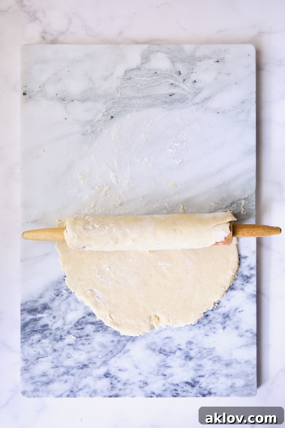 Galette dough being carefully rolled onto a rolling pin, demonstrating the technique for transferring it from a marble pastry board.
