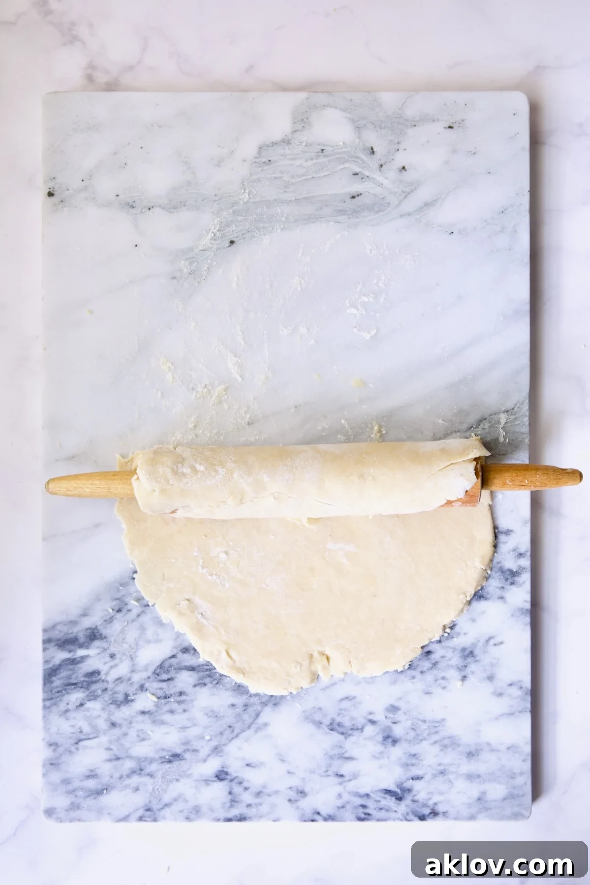 Galette dough being rolled onto rolling pin from marble pastry board.