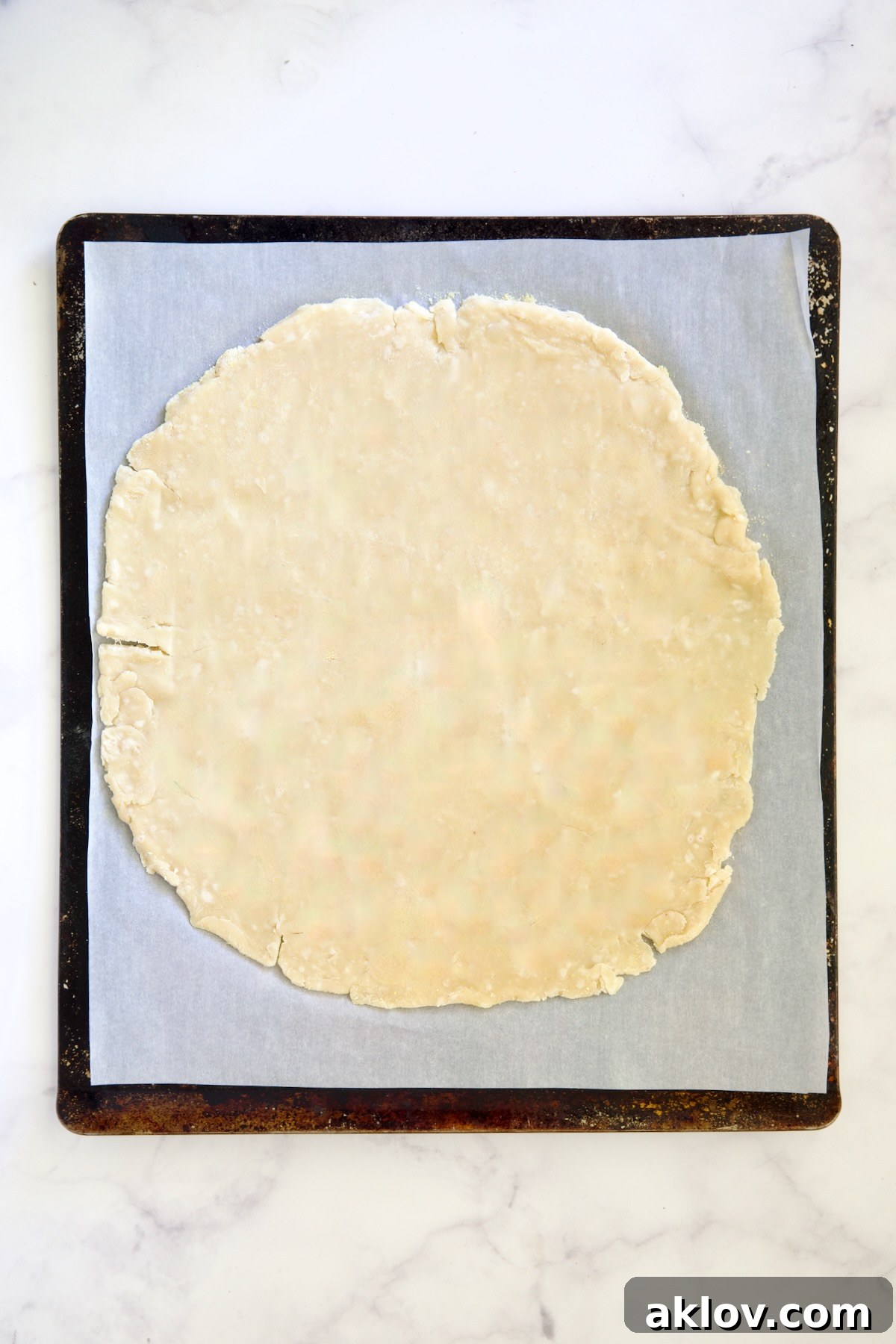 The rolled-out galette dough meticulously placed on a white parchment paper-lined baking sheet, awaiting its delicious filling.