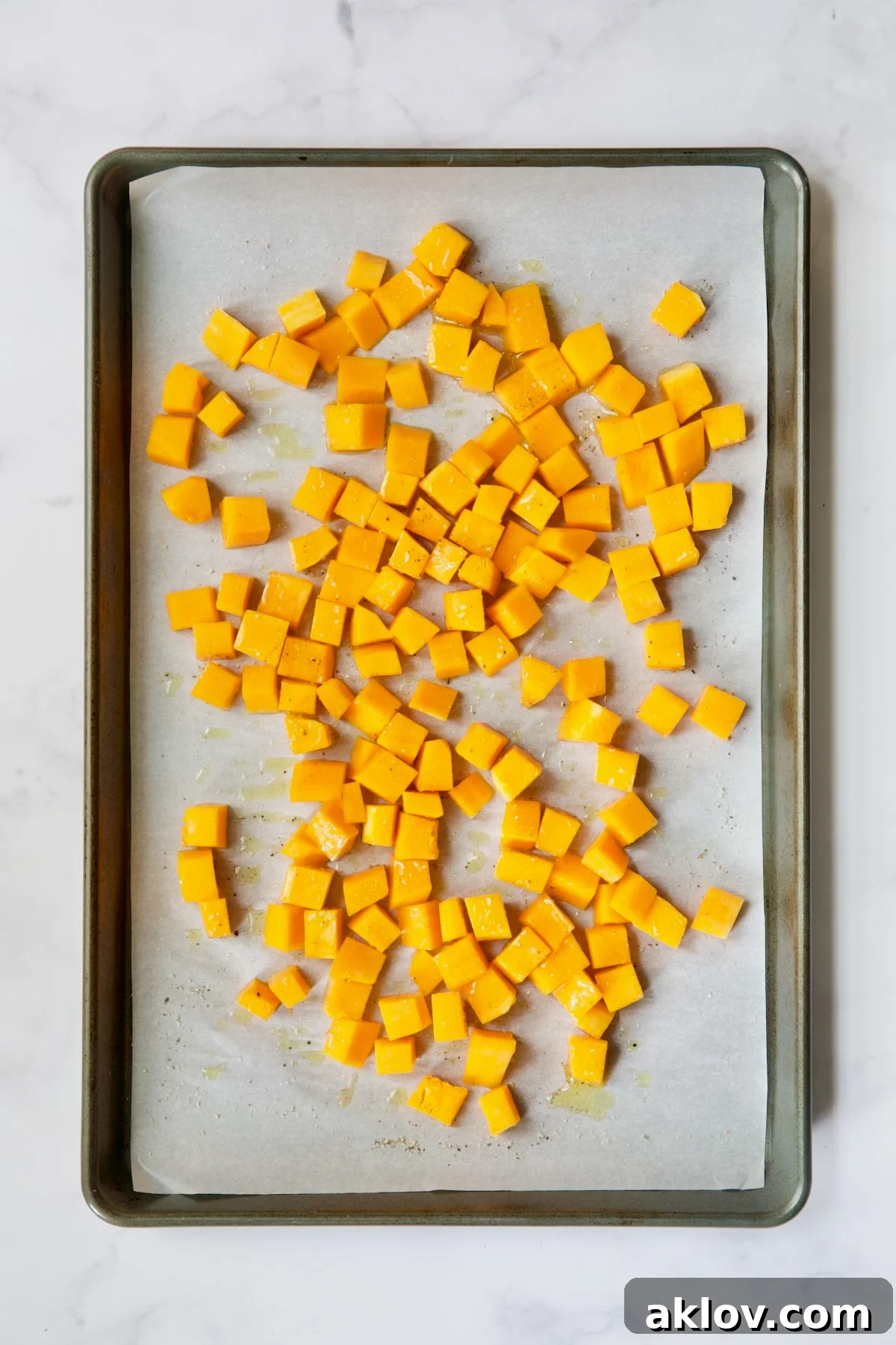 Butternut squash cubes on white parchment paper-lined baking sheet before being roasted.