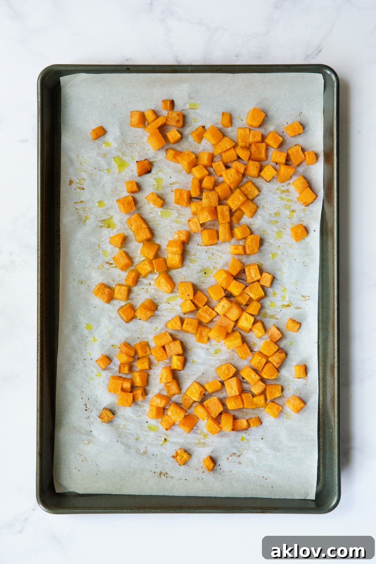 Roasted butternut squash cubes, golden and tender, arranged on a white parchment paper-lined baking sheet after baking.