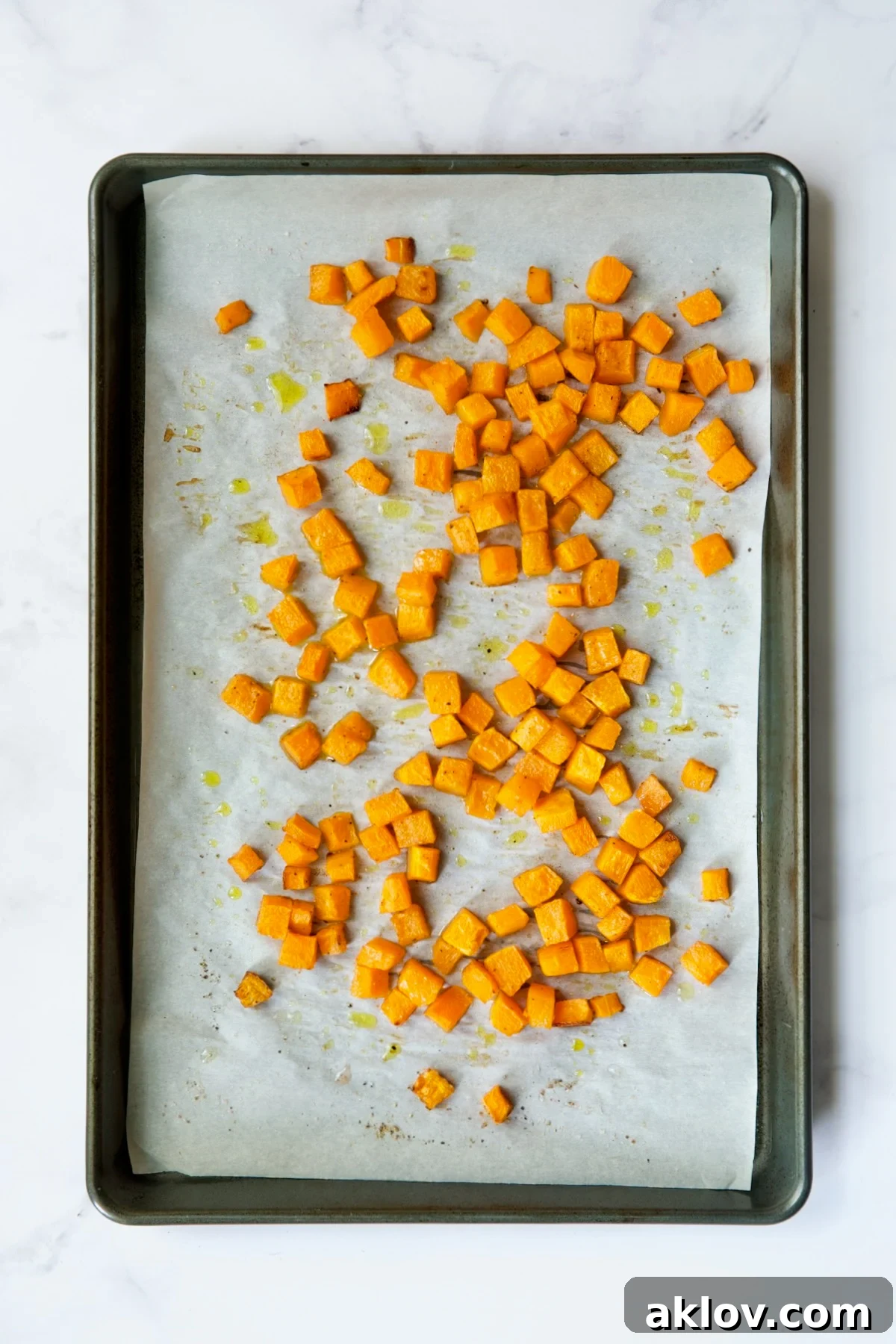 Roasted butternut squash cubes on white parchment paper lined baking sheet.