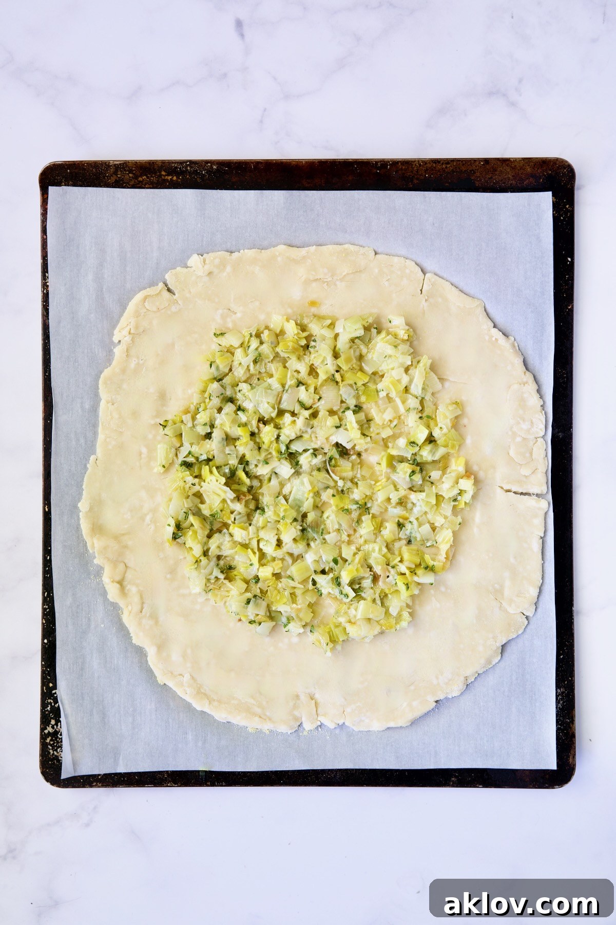 The foundation of the galette: a layer of tender leeks spread over the dough on a white parchment paper-lined baking sheet.