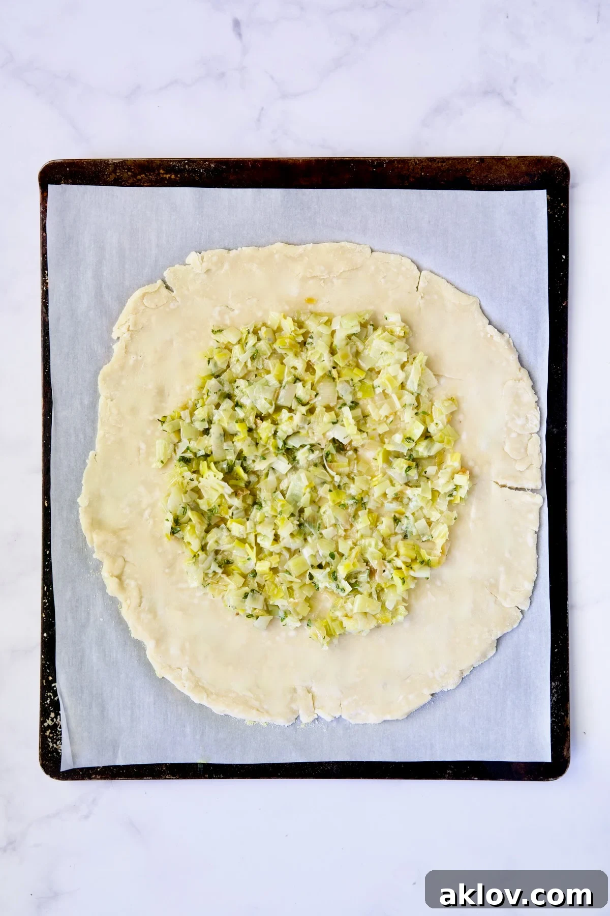 Leeks on galette dough on white parchment paper-lined baking sheet.