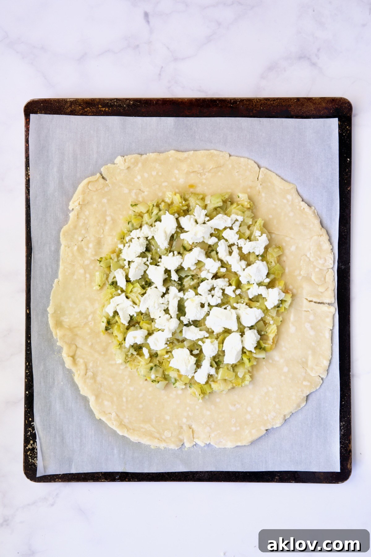 The delicious second layer: creamy goat cheese dotted over the leek mixture on the galette dough, all on a white parchment paper-lined baking sheet.