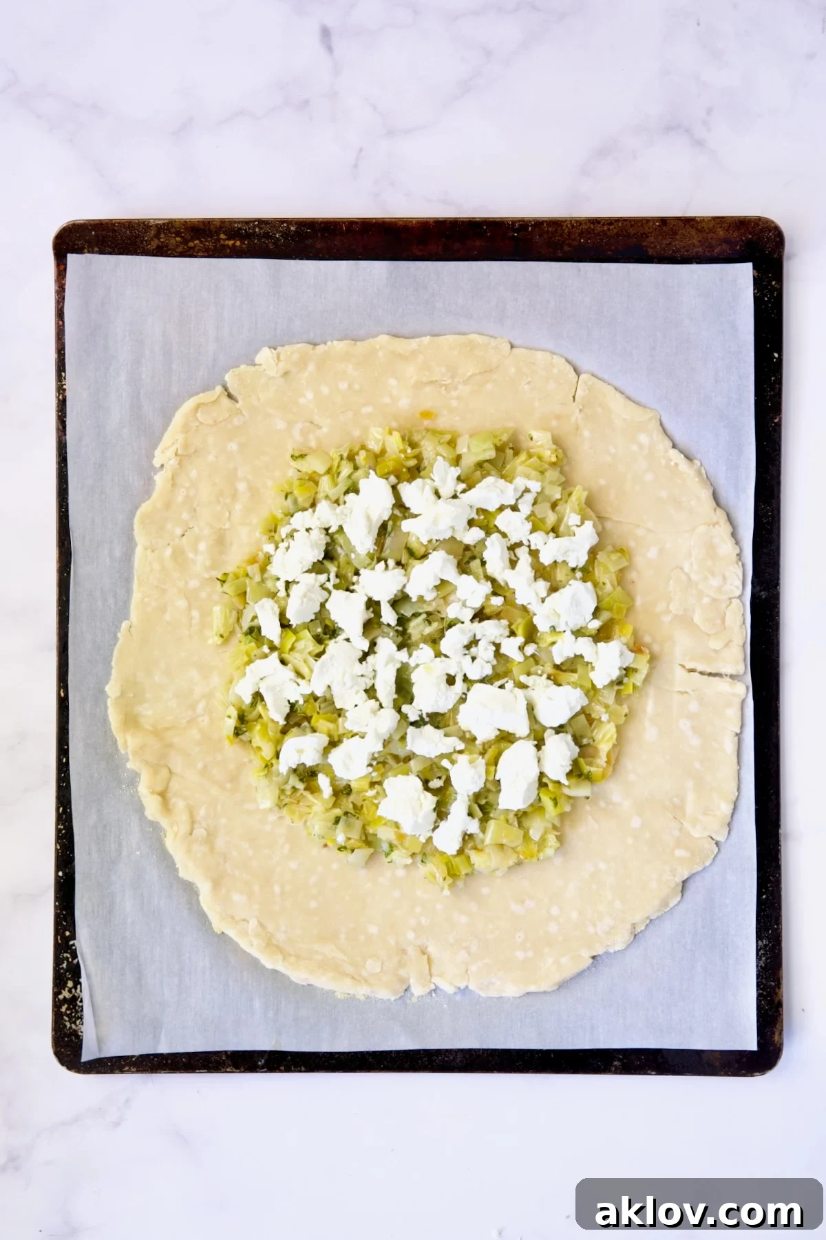 Leeks and goat cheese on galette dough on white parchment paper-lined baking sheet.