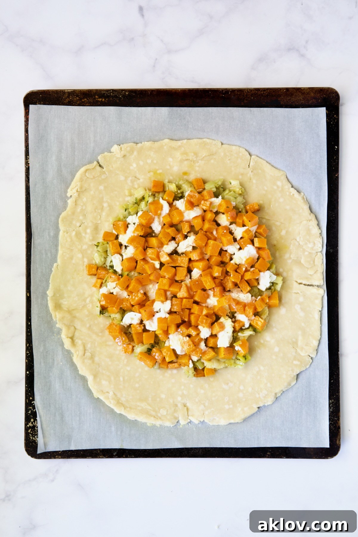 The final layer of the galette filling: vibrant butternut squash, creamy goat cheese, and tender leeks artfully arranged on the dough before the edges are folded.