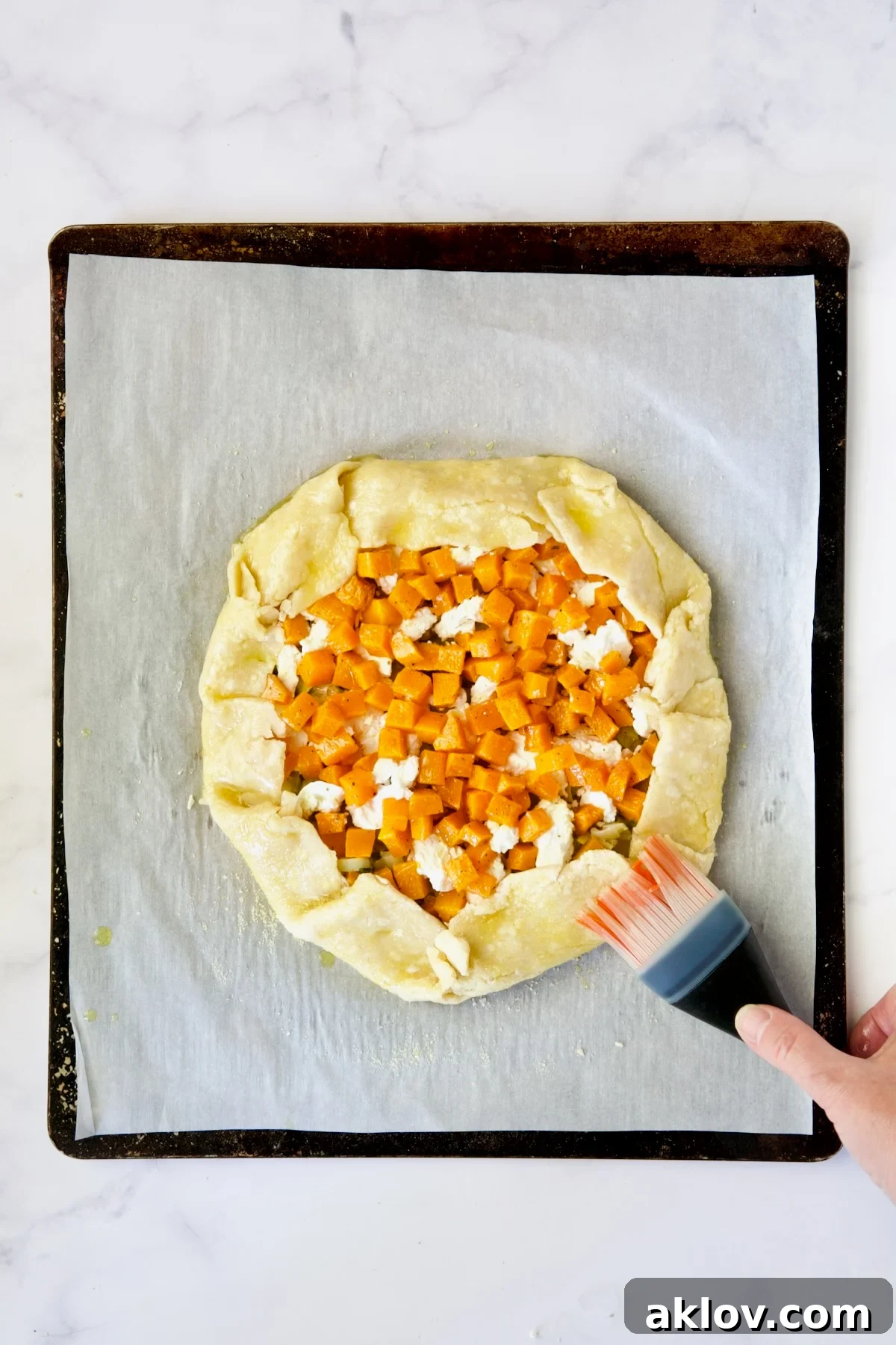 Assembled galette on white parchment paper-lined baking sheet being brushed with olive oil.