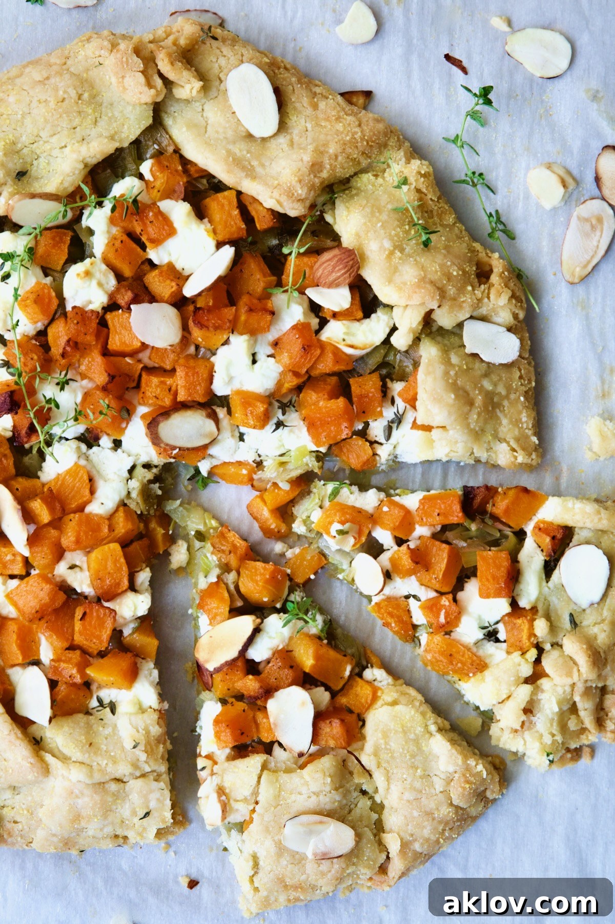 A stunning Butternut Squash, Leek, and Goat Cheese Galette presented on white parchment paper, elegantly garnished with toasted sliced almonds and fresh thyme sprigs.