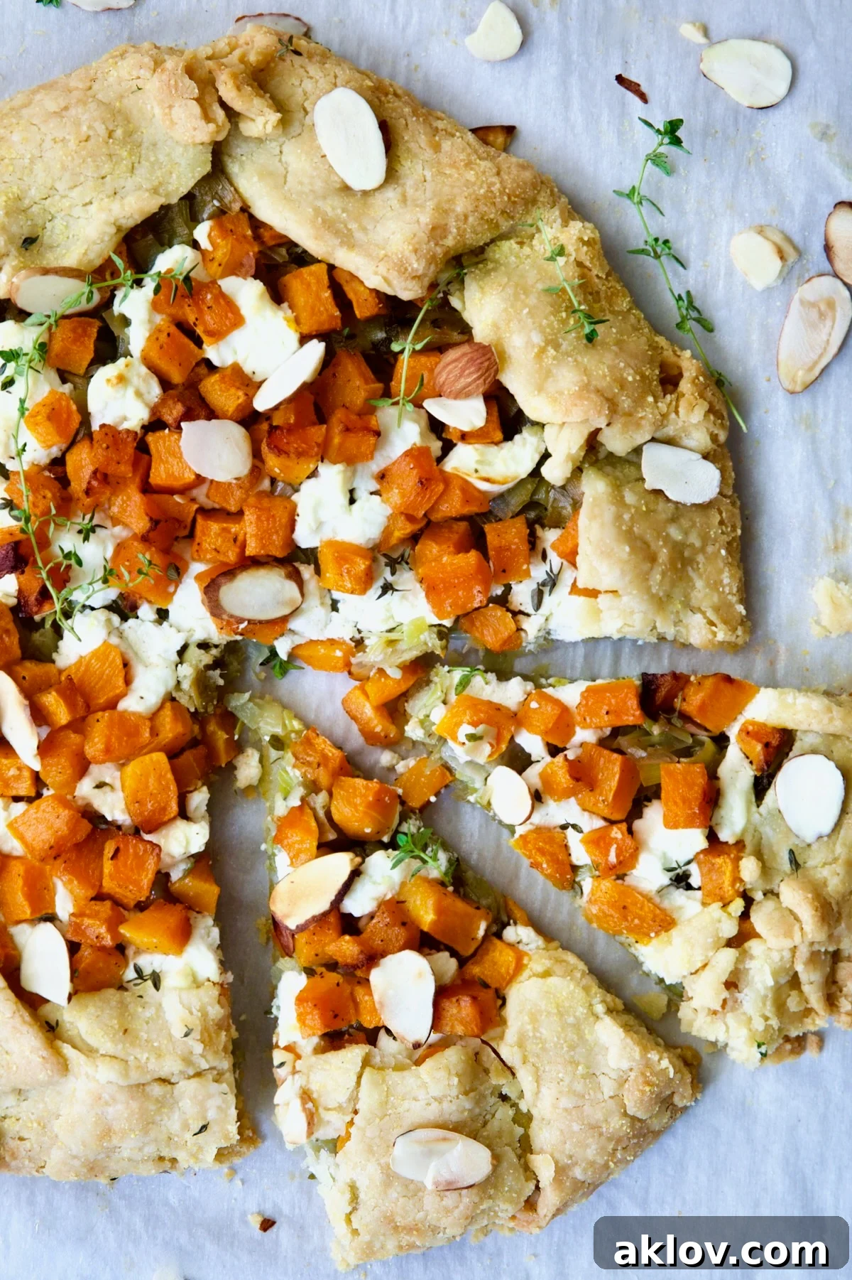 Butternut Squash Leek and Goat Cheese Galette on white parchment paper garnished with sliced almonds and fresh thyme sprigs.