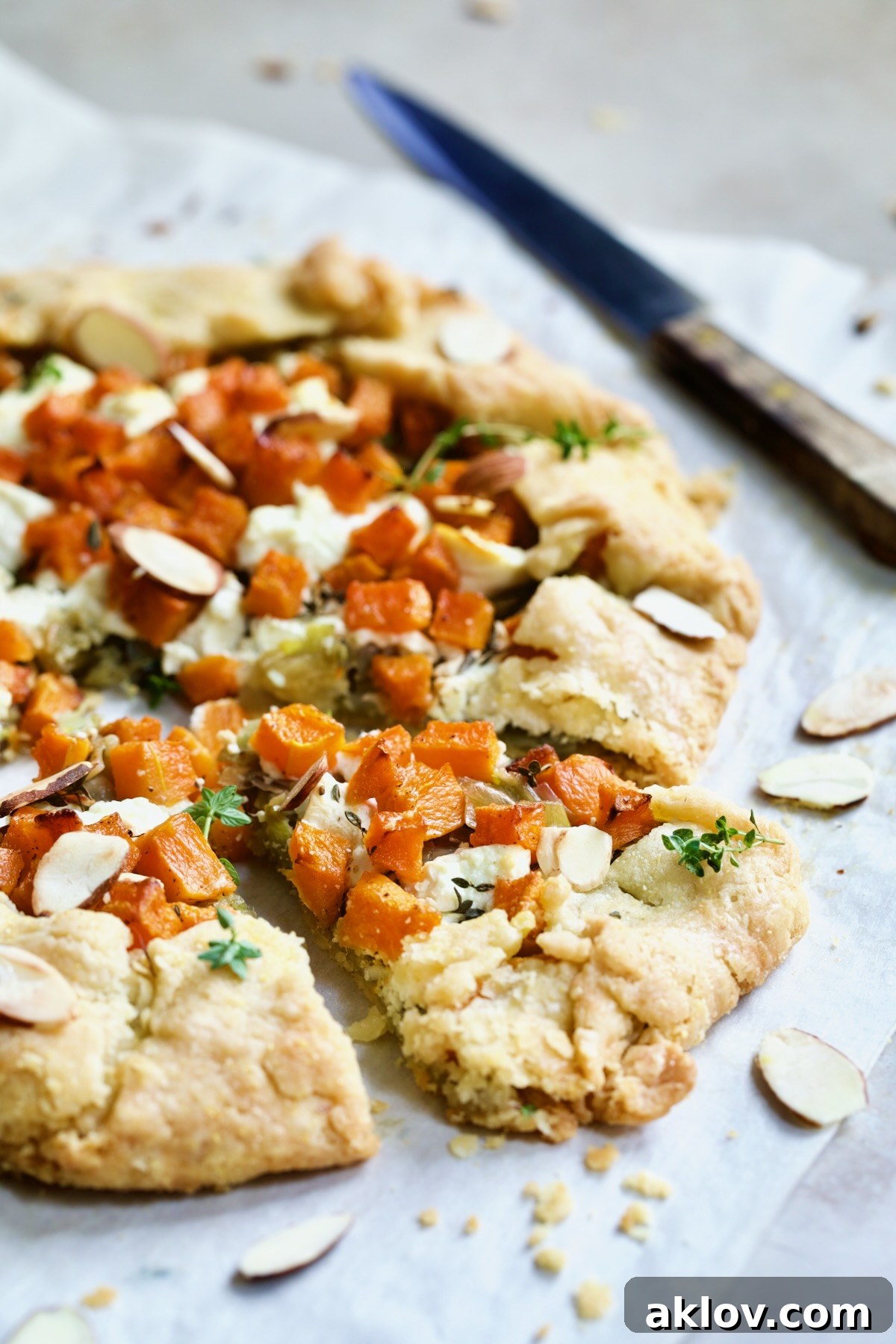 A beautiful Butternut Squash, Leek, and Goat Cheese Galette, elegantly sliced into wedges, garnished with toasted almonds, and ready to be served from a white parchment paper-lined baking sheet.