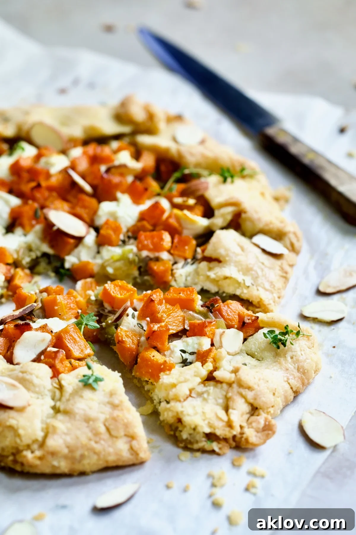 Butternut Squash Leek and Goat Cheese Galette on white parchment paper cut into wedges and garnished with sliced almonds.