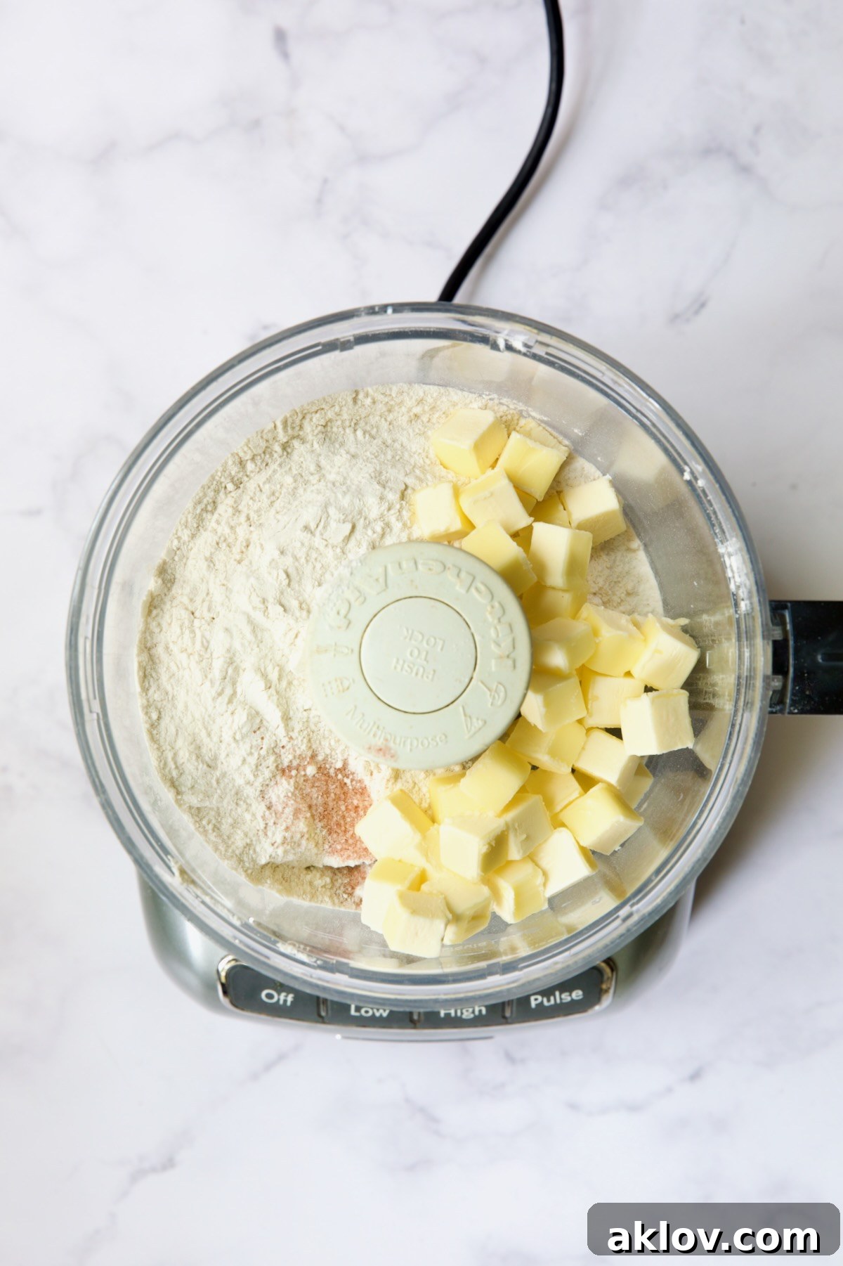 Cubes of cold butter, flour, and salt await processing in a food processor, ready for the initial steps of galette dough preparation.