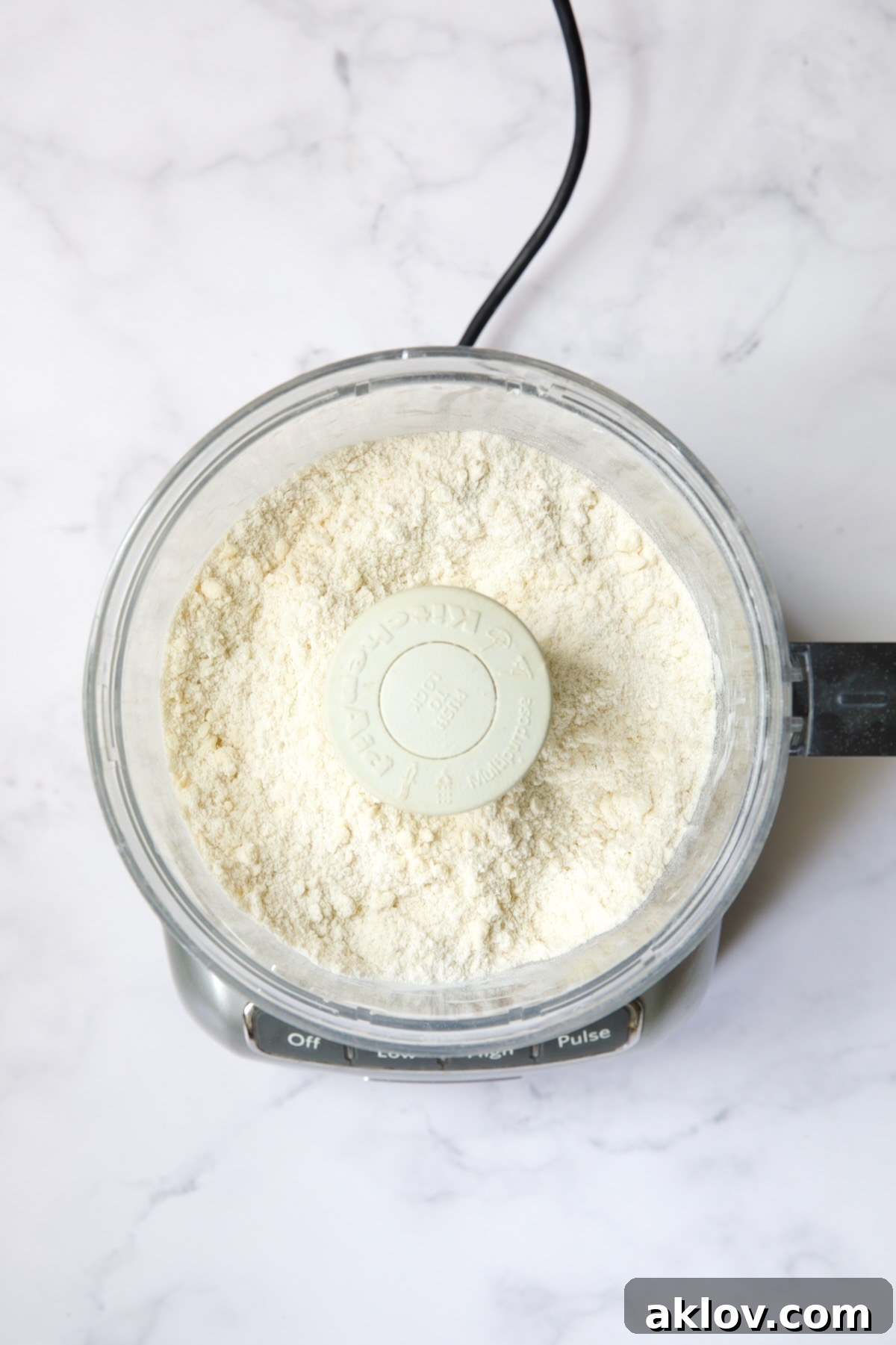 The galette dough ingredients in the food processor after the butter has been perfectly incorporated, showing a coarse, crumbly texture.