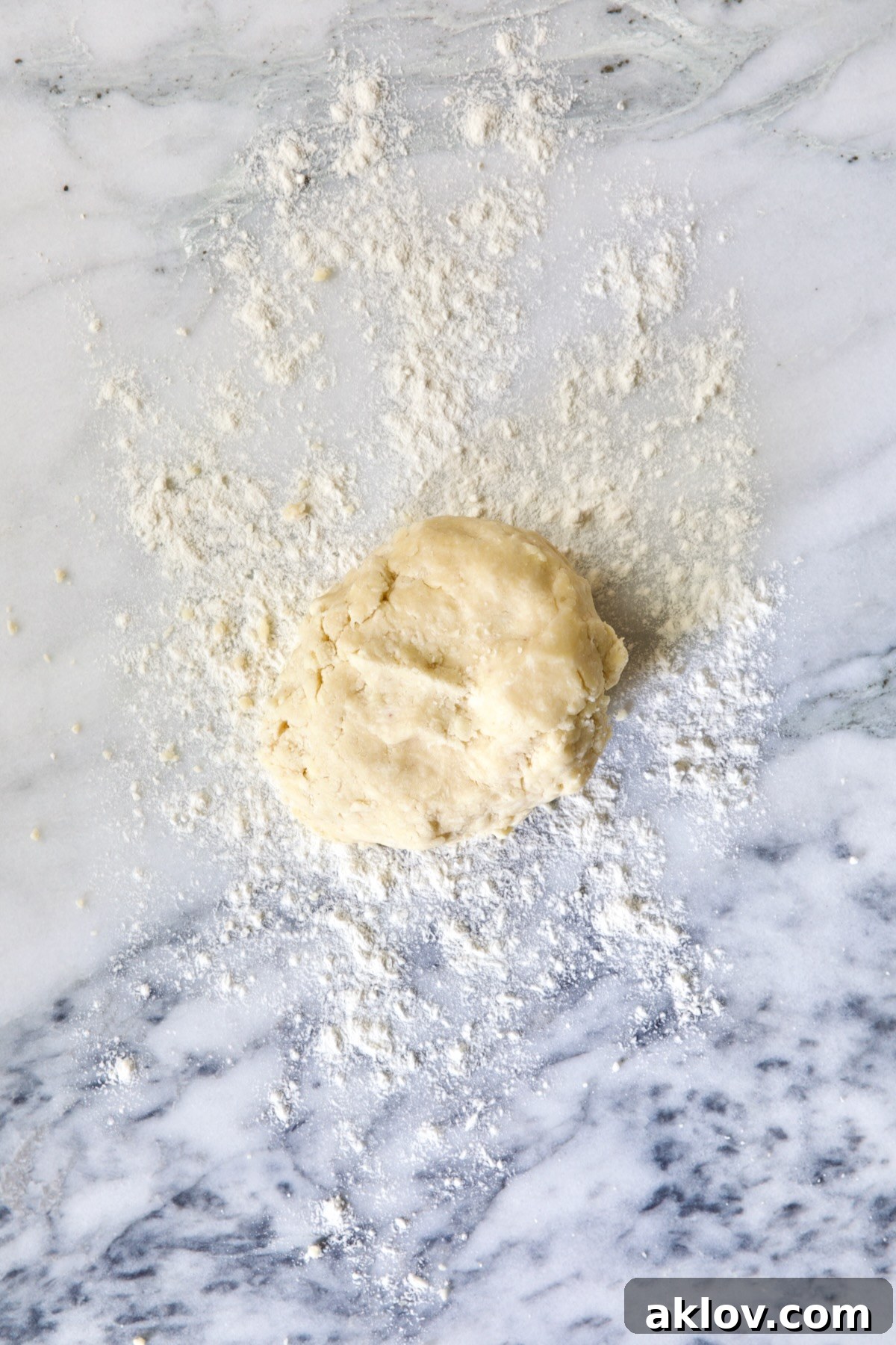 A perfectly formed ball of galette dough resting on a pristine white marble pastry board, awaiting the next step.