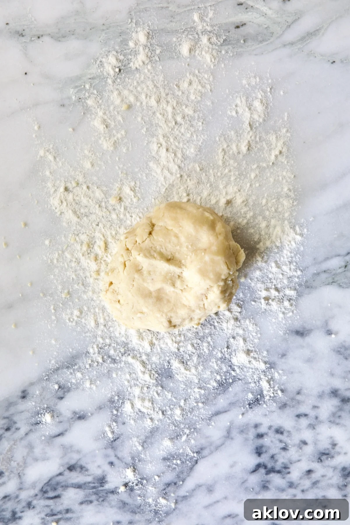 Ball of galette dough on white marble pastry board.