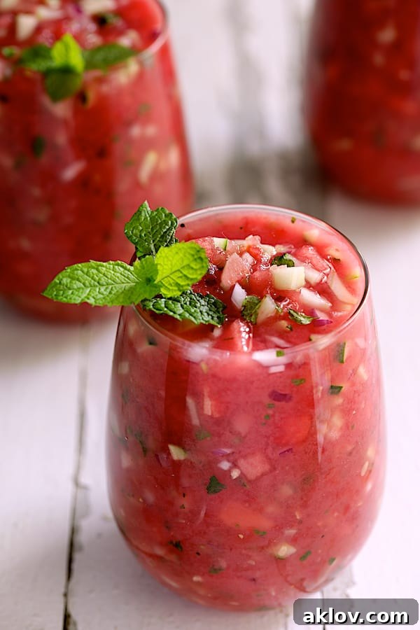 Vibrant Watermelon Gazpacho with Serrano Chiles and Mint served in elegant glasses, garnished with fresh mint sprigs, on a rustic white background, perfect for a hot summer day.