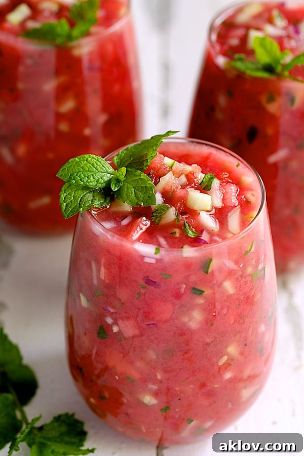 Three elegant glasses filled with vibrant Watermelon Gazpacho with Serrano Chiles and Mint, ready to be served on a pristine white background.